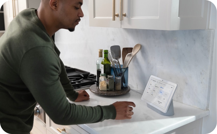 Person using a smart home control hub on a kitchen countertop to manage connected devices and home automation settings.