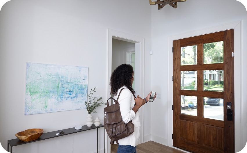 Person entering a home while using a smartphone, illustrating smart home device connectivity and compatibility.