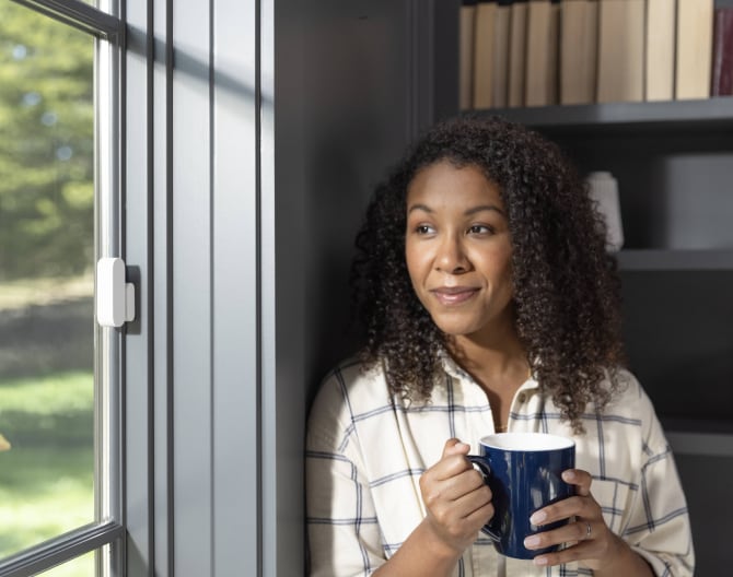 ADT customer standing next to her window that has a ADT Door/Window Sensor installed ADT customer standing next to her window that has a ADT Door/Window Sensor installed